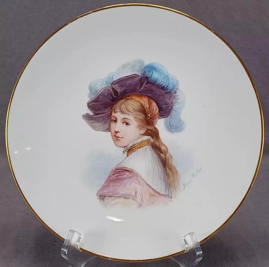 19th Century Paris Hand Painted Portrait Plate B: Nice antique porcelain plate. Decorated with a hand painted portrait of a Renaissance lady with a large blue feathered hat. Gold gilding along the edge. Signed by the Paris artist Georges Poitevin. Ha