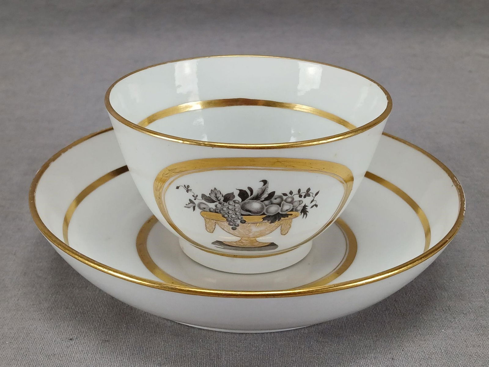 Thomas Wolfe Pattern No 91 Tea Bowl & Saucer: Antique British 19th century porcelain tea bowl and saucer. Decorated in the Thomas Wolfe / Factory Z pattern No 91 with bat print and gilt fruit basket in a gold ring. Gold gilding along the edge. Un