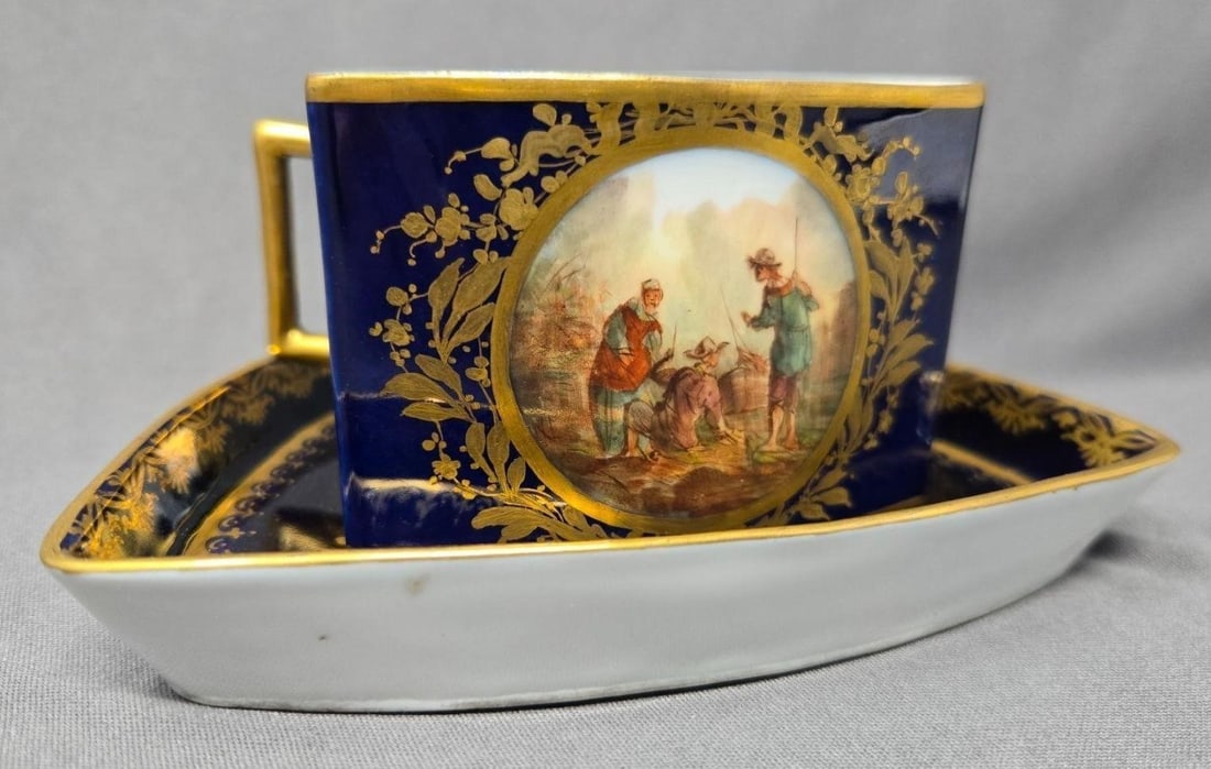 Vienna Style Triangular Cup and Saucer: Vienna style triangle shaped cup and saucer in a cobalt blue with gold flowers and accents. It has two hand painted fishermen and boat scenes. Very good condition with out chips or cracks or signs of