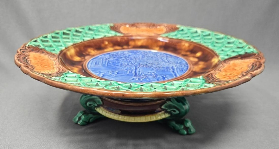 Wedgwood Majolica Footed Taza Reticulated C. 1875: Wedgwood majolica footed taza / compote. Courting scene with a couple on a bench with trees. The outside is reticulated with medallions of deer and a hunter. Stylized lions feet on stand. Very good co