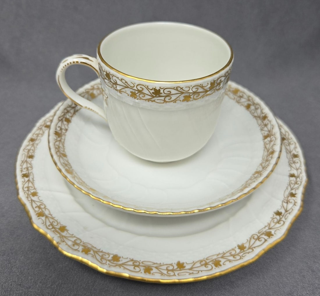 KPM Porcelain Trio: KPM green mark Porcelain trio with demitasse / mocha cup, saucer and dessert plate. Circa post 1913. Painted gold pattern on rim. Marked 70118. Very good condition without chips or cracks or scratches
