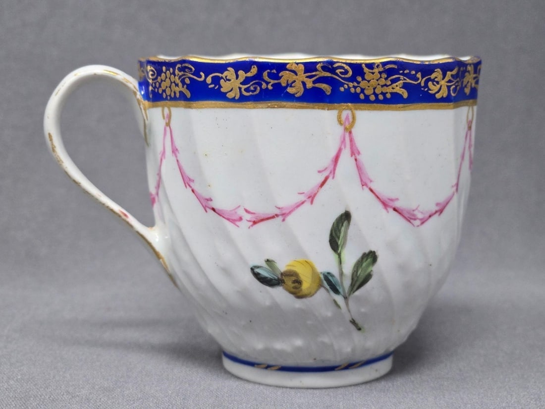 Share Old Darby Floral and Garland Teacup: Antique Darby teacup with a cobalt blue and gold rim, a pink swag and flowers. No Chips or cracks, there is some errant paint in spots. Measures approximately 2 1/2 inches tall and wide. Circa 1782 to