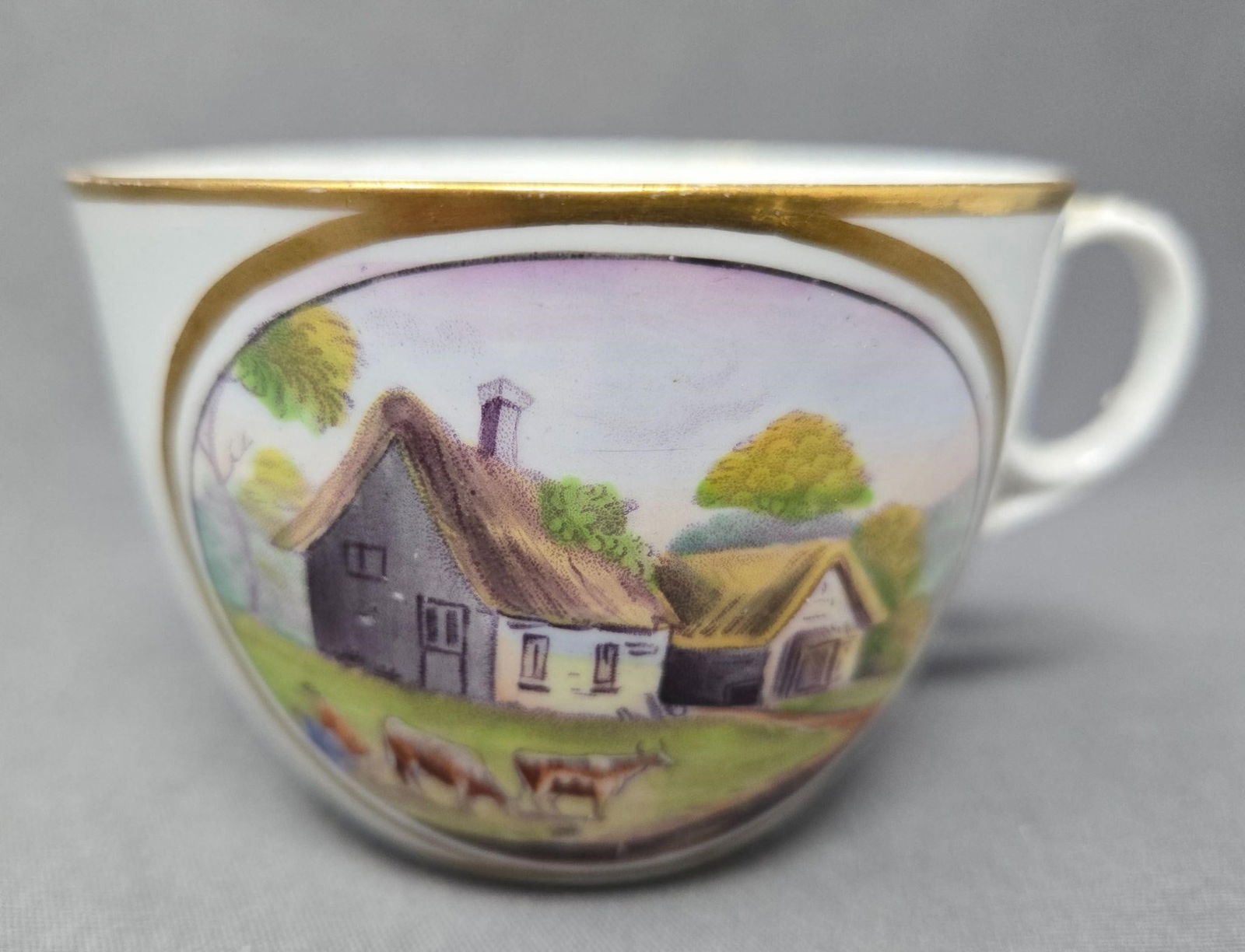 New Hall Pastoral Scenes Teacup C. 1810: New Hall teacup with two pastoral scenes. One has two woman and cows in front of a house the other has a man in front of a house. Circa 1800 to 1815. Bute shaped cup with an oval ring handle. No