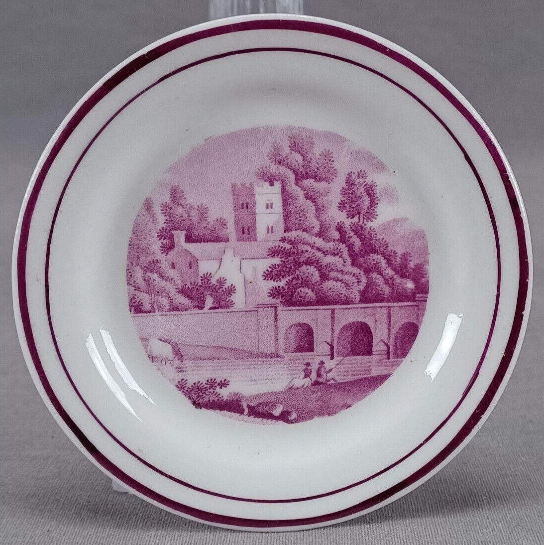 British Bat Print Tower Bridge Fishing Cup Plate: Nice antique British bone china cup plate. Decorated with a puce transfer scene showing a building with a tower, trees, a bridge, and men fishing. Double puce trim along the edge. Unmarked. Circa 1820