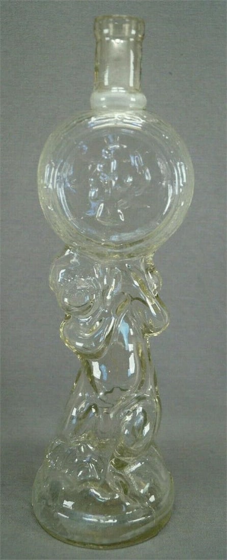 19th Century French Legras Cherub Liquor Bottle: Late 19th century French blown in mold glass liquor bottle of a cherub holding a round disk with a medallion. Unmarked. Attributed to Legras.Has some staining on the inside of the base, but otherwise