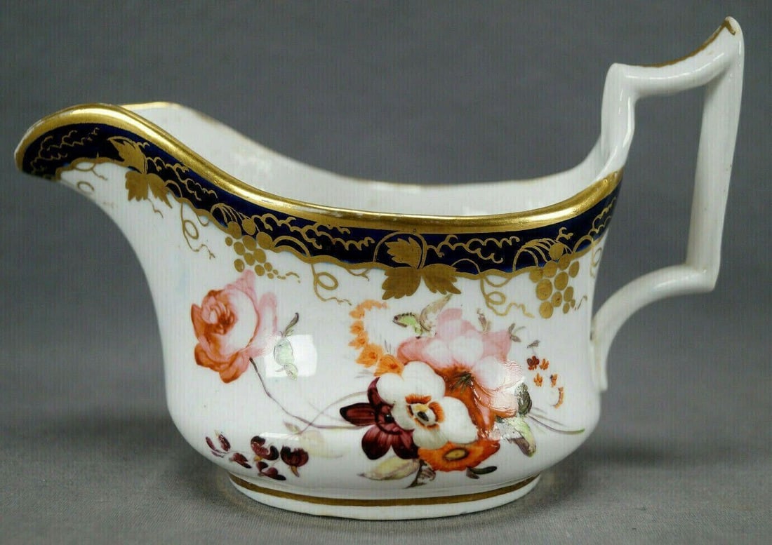 British Hand Painted Bone China Creamer C.1825-30: Nice British bone china creamer. Decorated with hand painted pink, purple, white, and orange flowers. With cobalt border with gold grape vine. The book the Cabinet of Creamers attributes this form to