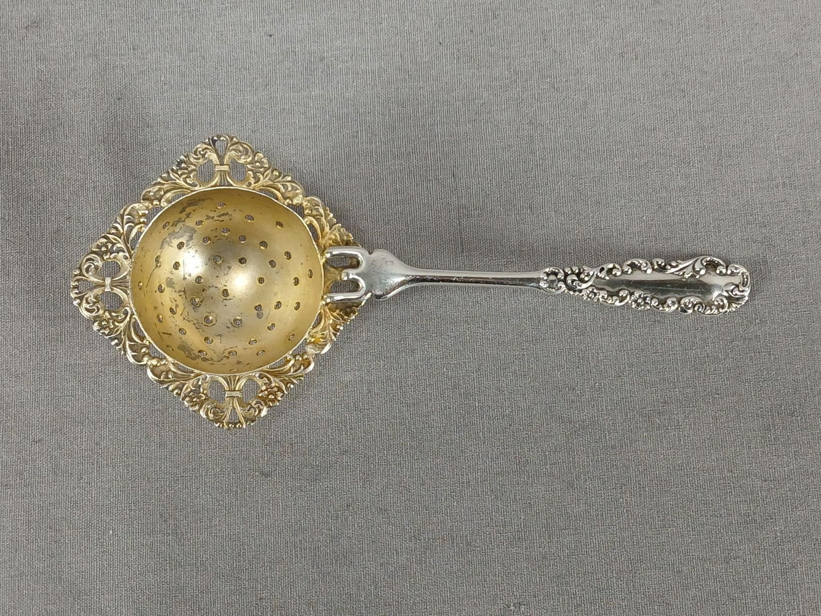 FS Gilbert Sterling Silver 5 1/2" Tea Strainer: Antique sterling silver tea strainer. Repousse scrollwork to the handle. Gold washed bowl. Marked G Sterling on the back of the handle for F.S. Gilber, North Attleboro, Mass, 1904 to 1915. Has wear an