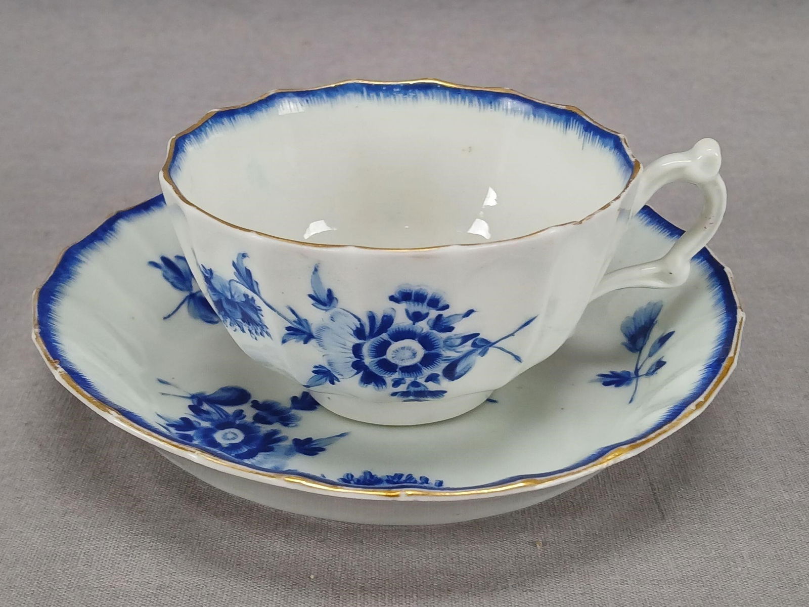 Dr Wall Worcester Blue Flowers Tea Cup & Saucer: Antique 18th century Dr Wall Worcester porcelain tea cup and saucer. Decorated with hand painted blue flowers. Has blue trim along the edge and gold gilding along the edge. Has an underglaze blue