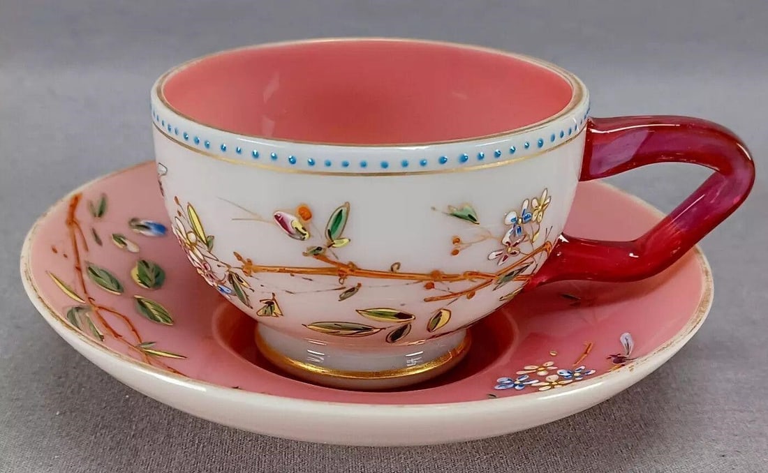 Harrach Bees Flowers Pink Opaline Tea Cup & Saucer: Nice antique Bohemian white cased pink opaline glass footed tea cup and saucer. With applied cranberry pink glass handle. The cup has small enameled blue beads along the lip. Both the cup and saucer a