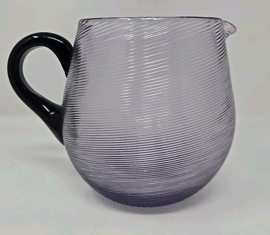 Victor Durand Ribbed Amethyst Pitcher: Victor Durand swirled molded ribbed pitcher with opaque black handle. Measures approximately 5 1/8 inches tall 6 3/4 inches long from spout to handle. 3 7/8 inches top diameter and 5 inches wide. No c