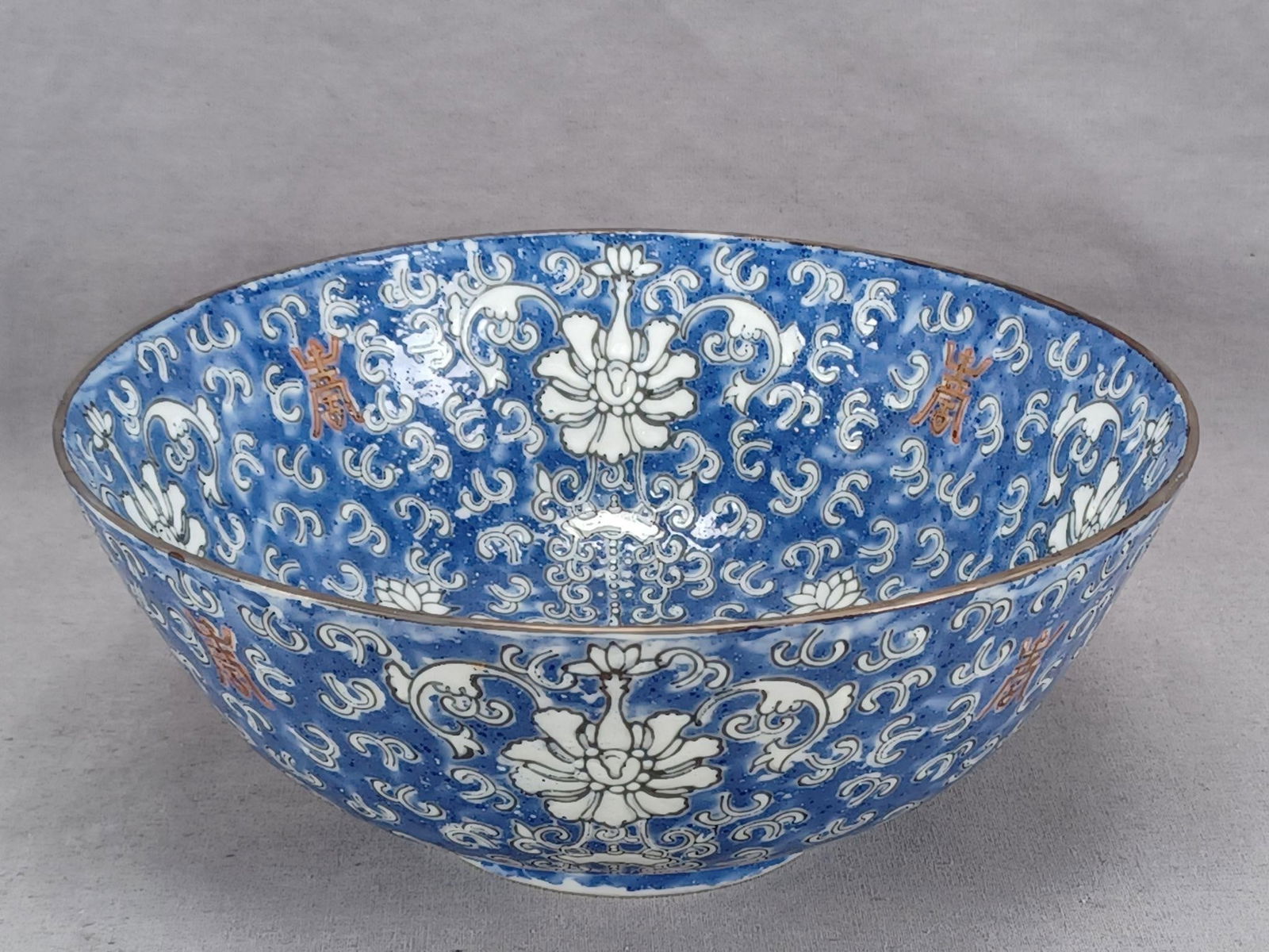 Chinese Chrysanthemum Shou Symbols Porcelain Bowl: 20th century Chinese porcelain bowl. Hand painted with a white chrysanthemum and Shou symbol pattern over a blue ground. Gold gilding along the edge. Has a red apocryphal Qianlong mark on the bottom.H