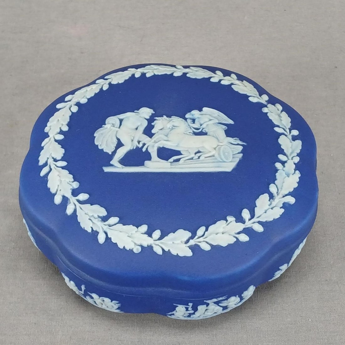 Wedgwood Dark Blue Jasperware 5 Inch Candy Box: British dark blue and white jasperware candy box. White applied sprigged Neoclassical figures and acorns. Impressed Made in England Wedgwood on the base.Good condition.Measures approximately 5 inches
