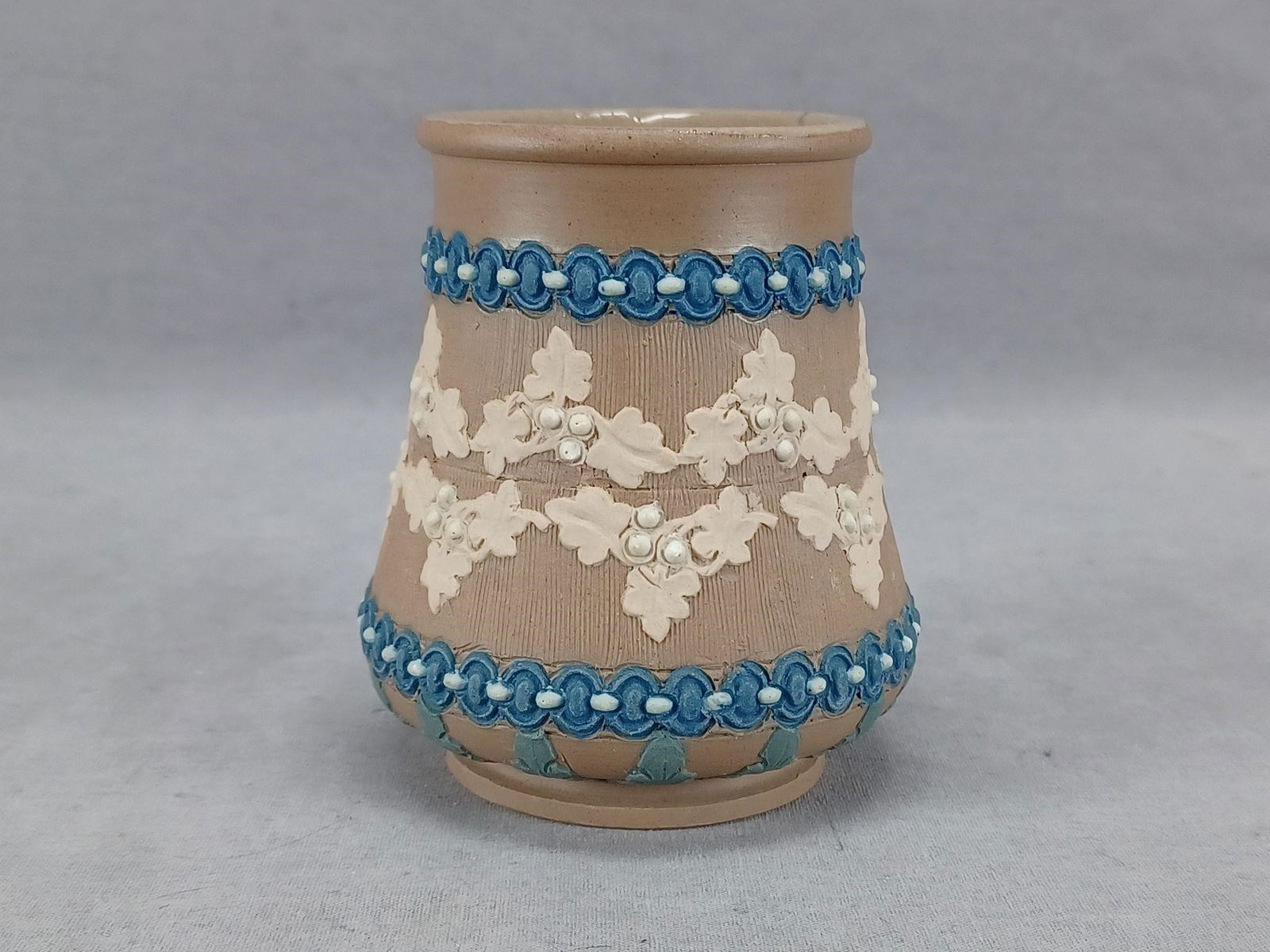 Doulton Lambeth Silicon Stoneware 3 5/8 Inch Vase: Antique British brown stoneware jug. With blue sprigged chain, cream berries, and leaves, and blue acanthus leaves. Marked Doulton Silicon Lambeth. This is an impressed mark used on Silicon wares betw