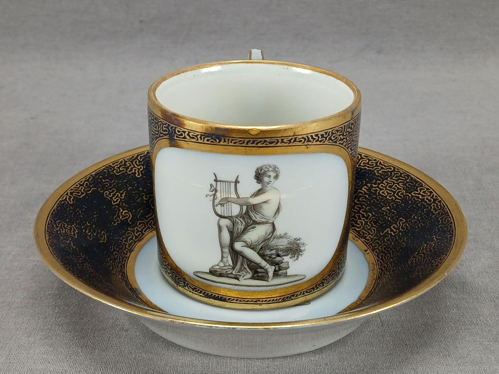 KPM Berlin Neoclassical Cobalt Cup & Saucer C.1790: Antique German porcelain coffee can or cup and saucer. Decorated with hand painted Neoclassical figures framed in gold gilding. Has gold vermicelli gilding over a cobalt blue background. Gold gilding