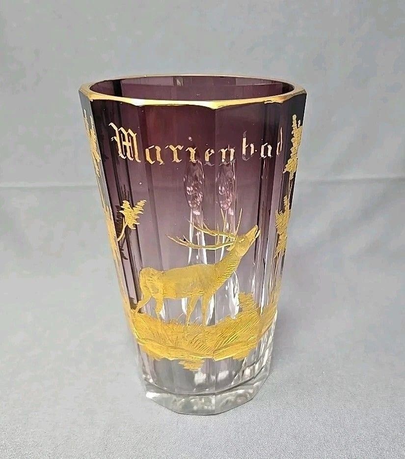 Bohemian Measuring Cup Drinking Glass with Stag: Marienbad souvanier drinking glass / measuring cup. It is purple that fades to clear with and etching, painted in gold with a stag and trees. There is an applied glass handle. Optic molded. There are