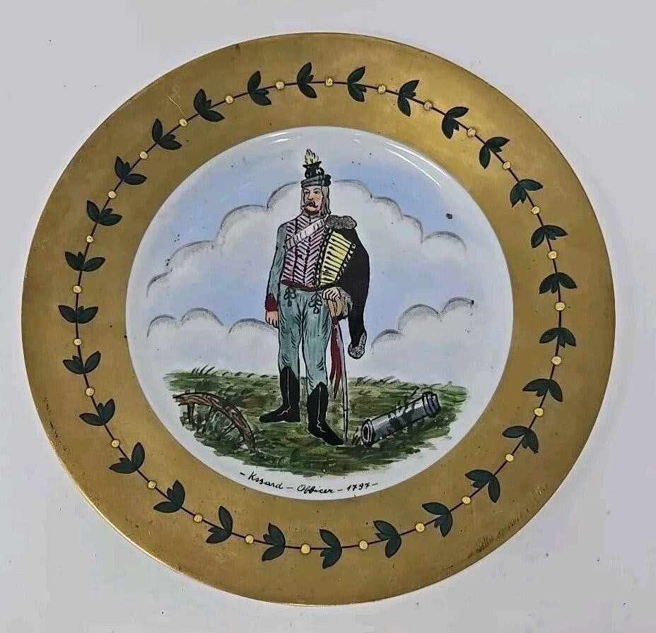 Napoleon Era Officer Porcelain Plate, French: Unmarked French porcelain plate depicting a Napoleonic era officer. Circa 1860s. Hand painted with a laurel on heavy gold border with enamel jeweling and the center has a soldier standing in a battle