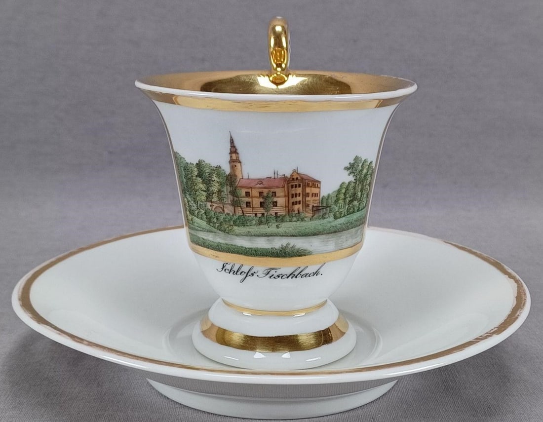 KPM Berlin Schloss Fischbach Cup & Saucer C. 1820s: Antique German porcelain empire form cup and saucer. The cup is decorated with a hand painted topographical scene framed in gold gilding. Has the name of the scene, Schloss Fischbach, in black below t