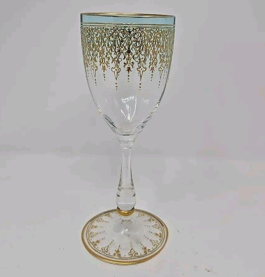Bohemian Gold Scrollwork Blue Wine Glass: Bohemian wine glass with gold scrollwork in blue that fades to clear. The scrollwork is a heart design with fleur de lis. It has light optic molding and a smooth bulbous stem. Measures approximately 6
