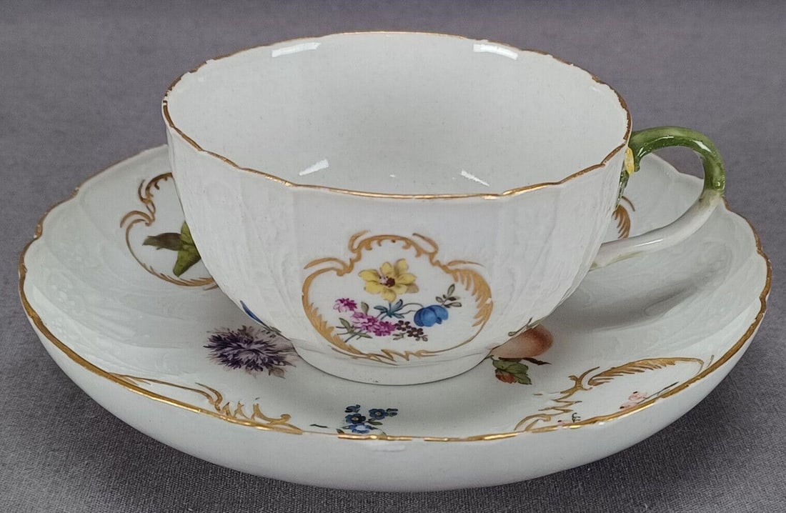 Meissen Fruits Floral Tea Cup & Saucer C1740: Nice antique 18th century German porcelain tea cup and saucer in the New Dulong pattern moulding. Decorated with hand painted fruits and flowers. With smaller flowers in gold scrolls. Gold gilding alo