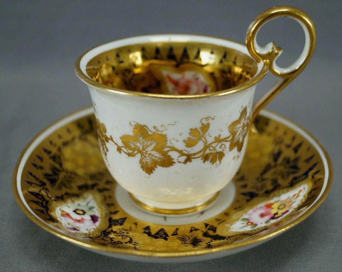 Coalport Hand Painted Floral Cup & Saucer C1815-25: Nice British Coalport bone china cup and saucer. Decorated with a gold grape vine on the outside of the cup. With a cobalt border with gold gilt grape vine overlay and hand painted flowers in pink,