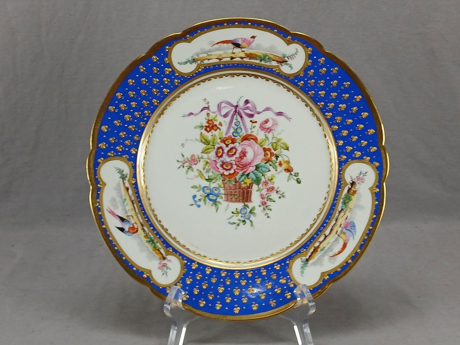 Sevres Style Hand Painted Floral Birds Plate B: Antique late 19th century or early 20th century French porcelain plate. Decorated with a hand painted floral basket with a purple bow in the center. Has a border of hand painted birds and flowers over