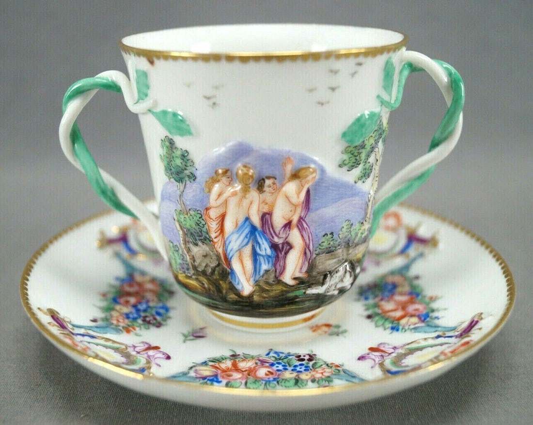 Ginori Capodimonte Double Handle Cup & Saucer: Nice 19th century entwined double handle chocolate cup and saucer. Decorated in the Capodimonte style with relief molded and hand painted figures , a dog, and trees. The saucer is decorated with flora