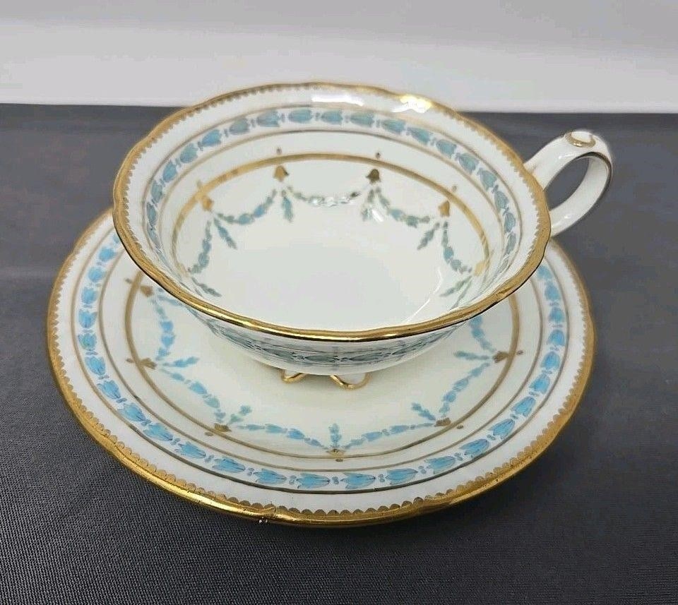 Cauldon Teacup & Saucer England NY Retailer: Cauldon Ltd cup and saucer set, Stoke on Trent England. Blue flowers garland and band with gold details. Molded foot and handle and lightly scalloped edge. No chips or cracks, light scratches from use