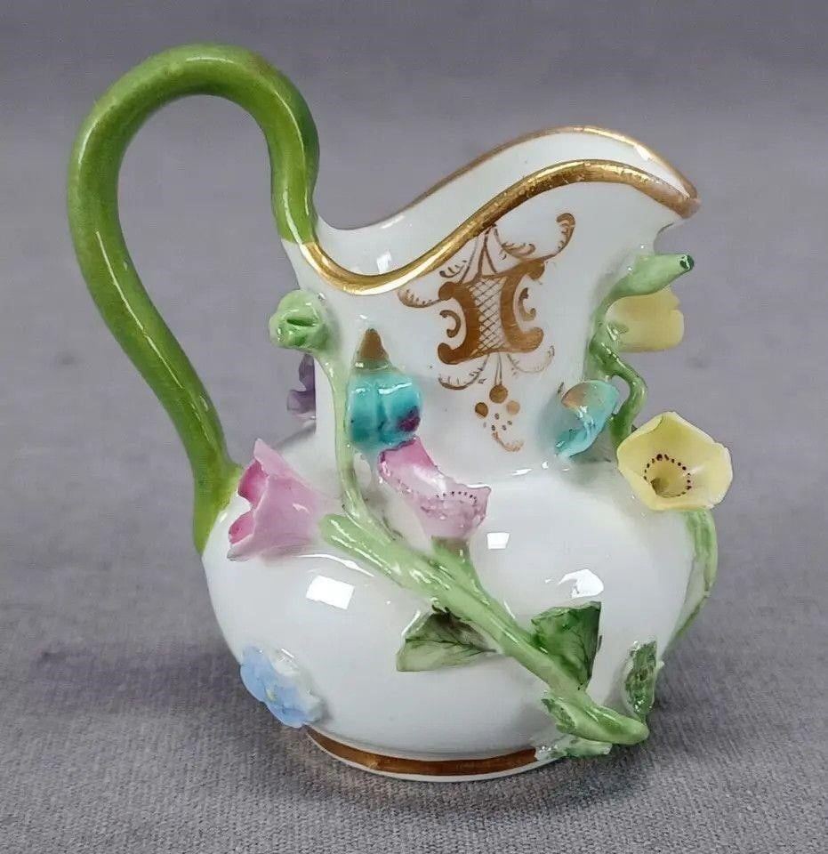 Coalbrookdale Style Floral Encrusted Mini Creamer: Antique British Coalbrookdale style bone china miniature creamer. Decorated with encrusted flowers painted in purple , pink, blue, and yellow. With gold scrollwork highlights and gold gilding. Green h