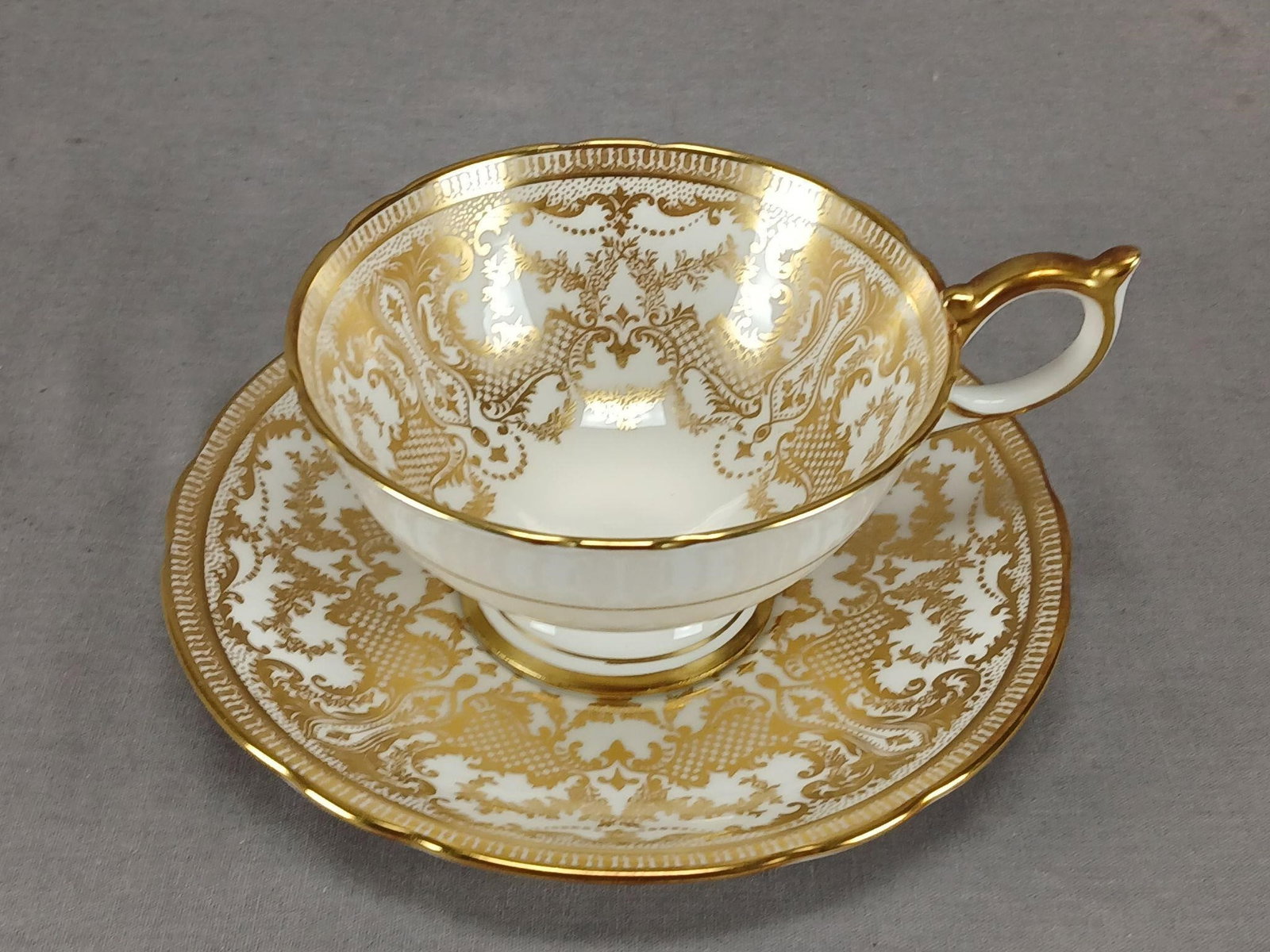 Aynsley Gold Floral Scrollwork Tea Cup & Saucer: Nice vintage British bone china tea cup and saucer. White with a gold band on the outside of the cup. Decorated with gold floral, scrollwork, and lattice pattern on the inside of the cup and on the sa