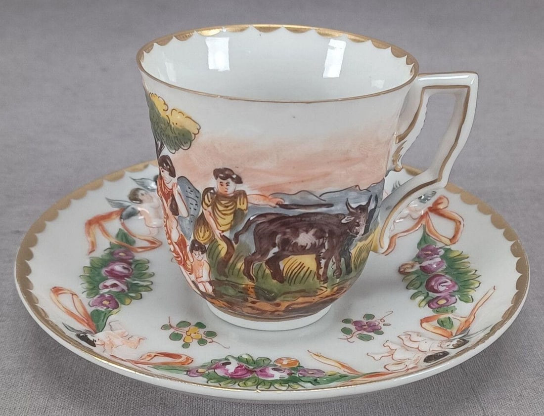 Antique Capodimonte Style Demitasse Cup & Saucer: Nice antique late 19th century German Capodimonte style porcelain cup and saucer. With relief molded and hand painted Neoclassical scenes on the cup and cherubs with rose swags on the saucer. Gold hig