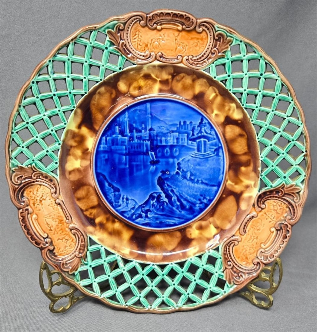 Wedgwood Majolica Reticulated Plate, City Scene: Wedgwood Majolica plate. It has a reticulated edge with a blue pastoral scene in the center and three medallions with deer and a hunter. The date code is R for 1863. Left the Sotheby's sticker on for