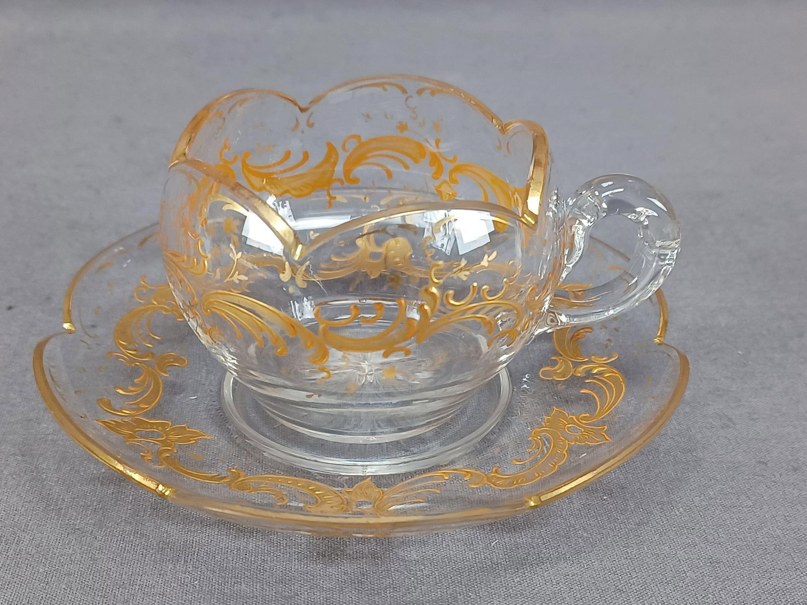 Josephinenhutte Raised Gold Glass Cup & Saucer: Nice antique hand blown clear scalloped edge glass cup and saucer. Decorated with a raised gold floral scrollwork pattern. Gold gilding along the edge. Star cut base. Unsigned. Probably produced by Jo