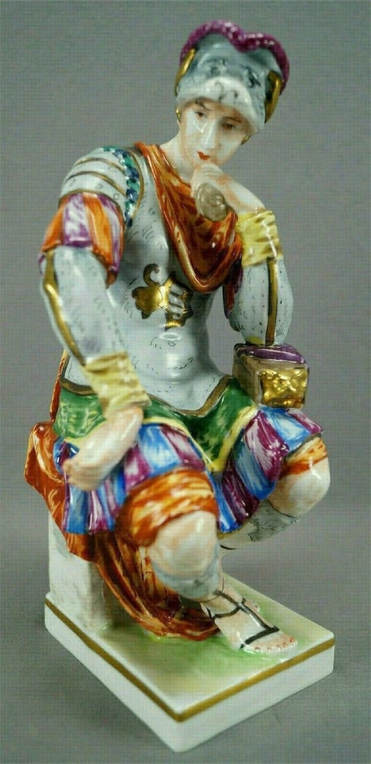 Carl Thieme Dresden Tomb Lorenzo Medici Figurine: Rare porcelain figurine of a seated soldier with an animal head helmet. He is painted in multiple in shades of blue, orange, pink, green, yellow and gold gilt. He is holding something in his hand and 