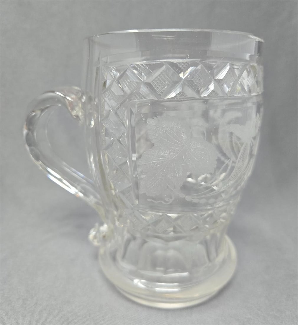 Bohemian Cut and Etched Floral Mug Late 1800s: Bohemian cut glass with etched design with grapes leaves and flowers. Diamond cuts with cross hatch around etched design and panel cuts at base. Honest wear on the bottom and some discoloration where 