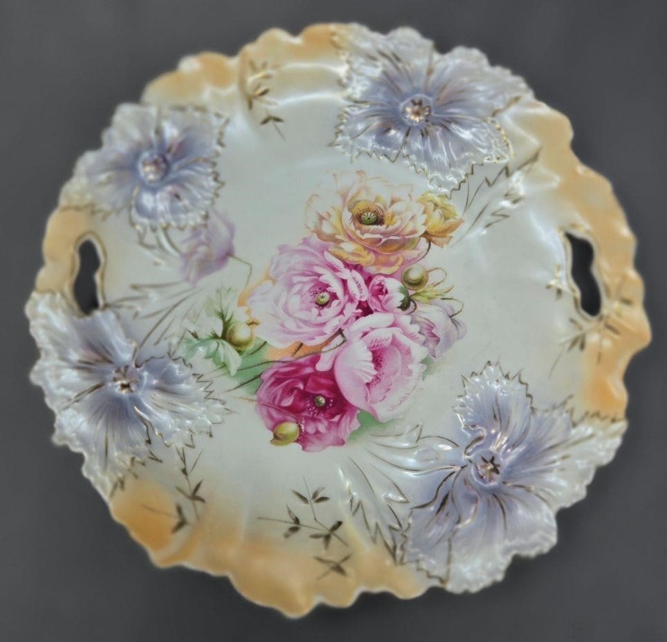 RS Prussia Handled Plate Carnations Mold 28: RS Prussia mold 28 handled dessert plate. It has 4 lavender molded carnations on the border and primroses in the center. Very nice condition with no chips or cracks and only seeing one minor rub as we