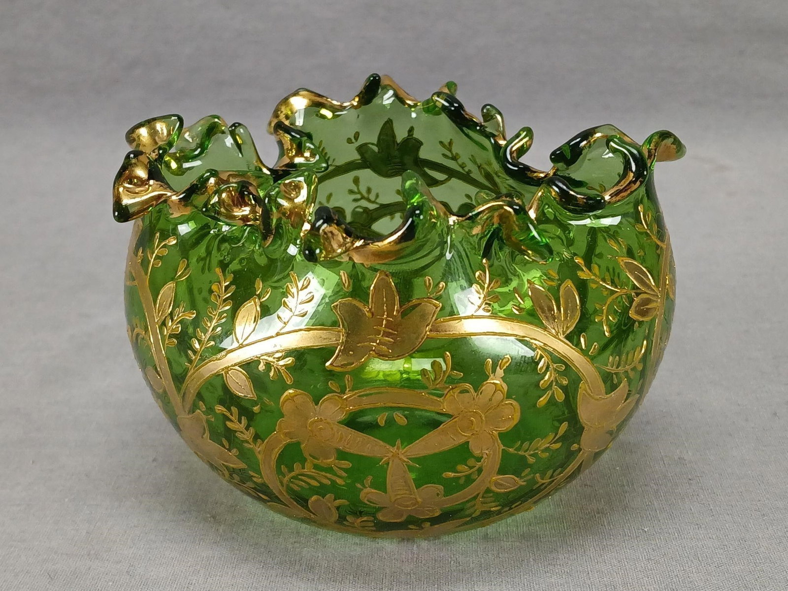Antique Bohemian Gold Floral Green Glass Bowl: Antique Bohemian blown green glass bowl. Decorated with raised gold floral scrollwork. Has a crimped rim with gold highlights. Ground and polished pontiled base. Unsigned. Has wear to the gilding,