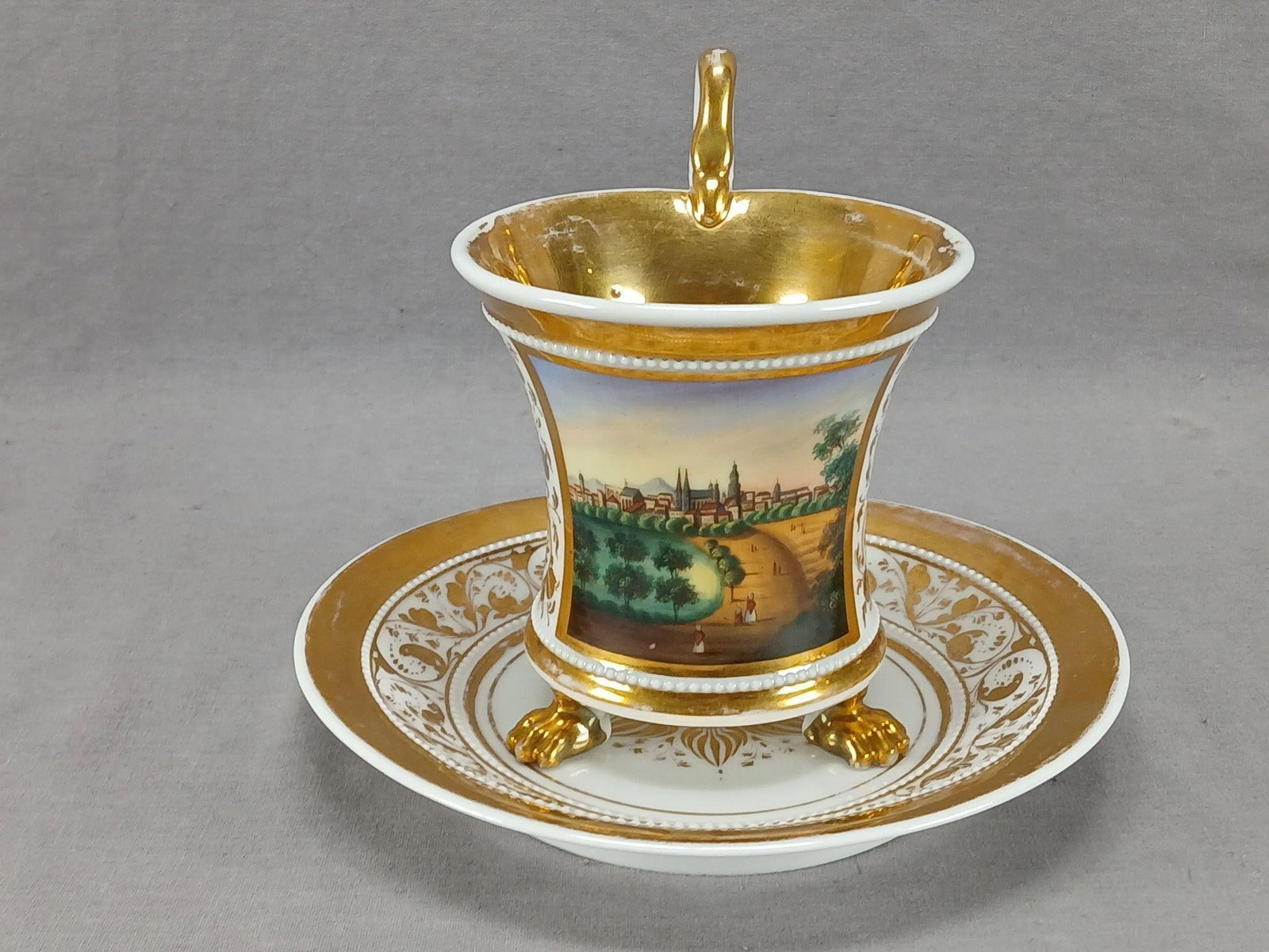KPM Berlin Thale Empire Form Cup & Saucer: Antique German porcelain empire form cup with figural swan handle, white beading, and three gilt feed. The cup is decorated with a hand painted scene framed in gold gilding. With gold floral scrollwor