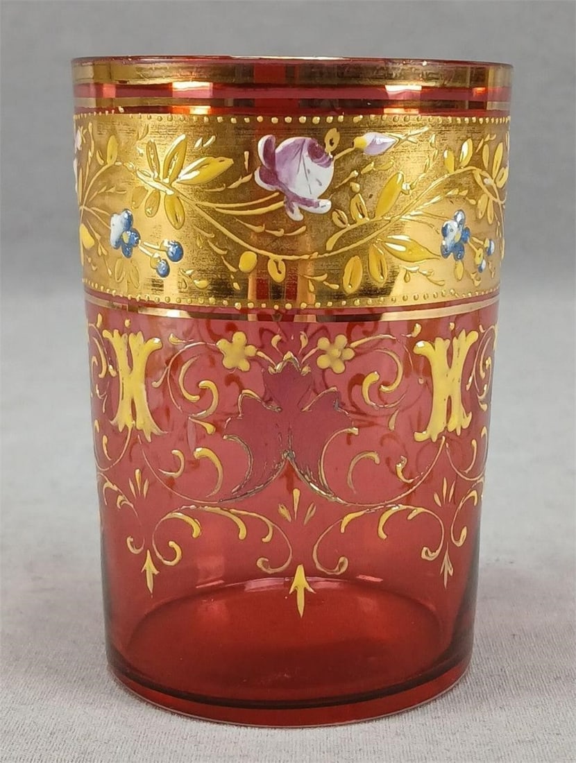 Harrach Enameled Floral Cranberry Glass Tumbler: Antique Bohemian blown cranberry glass tumbler. Decorated with hand enameled pink rose and blue forget me nots with yellow and gold leaves over a gold band above yellow floral scrollwork and H designs