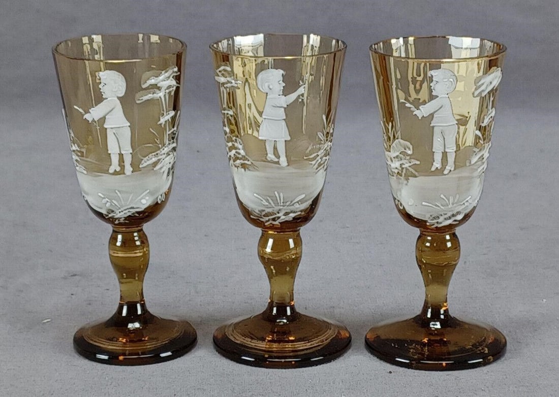 3 Mary Gregory Enameled Amber Glass Cordials: Set of 3 antique Bohemian optic molded amber glass cordials. Decorated in the Mary Gregory / Snow glass style with hand enameled children and flowers in white. Gold gilding along the edge. Unmarked. C