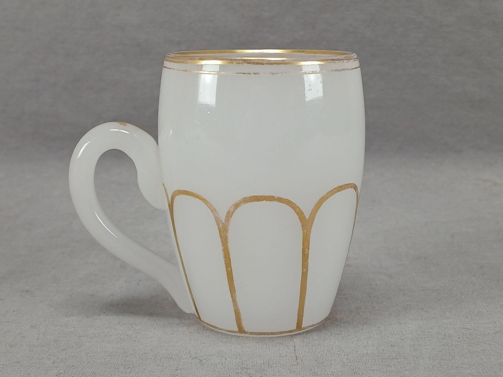 Bohemian Alabaster Glass & Gold Mug Circa 1850s: Antique 19th century Bohemian white opaline alabaster glass mug with applied glass handle. Gold gilding along the rim. Gilt paneled pattern around the bottom half of the mug. Gold gilding down the cen