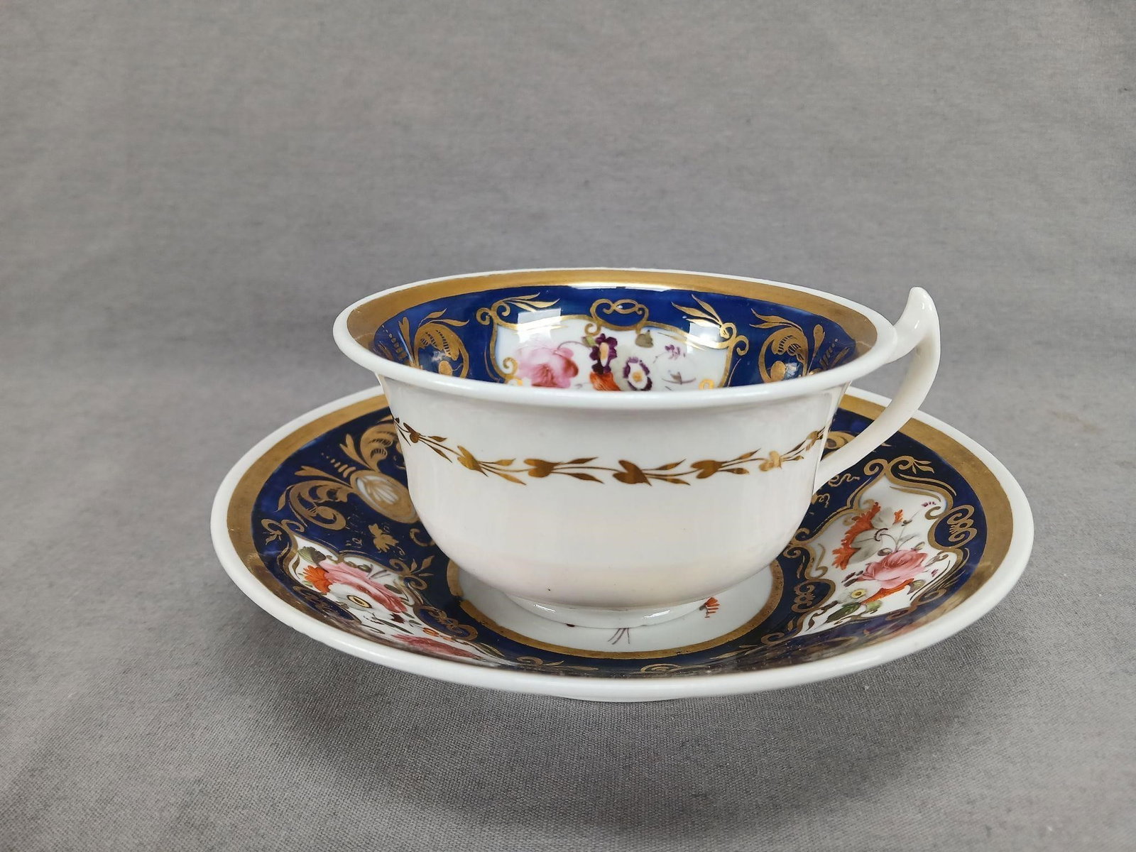 Coalport Hand Painted Tea Cup & Saucer C.1817-1825: Antique British bone china tea cup and saucer. Has a gold leaf band on the outside of the cup. Decorated on the inside of the cup and on the saucer with hand painted flowers in pink, orange, and purpl