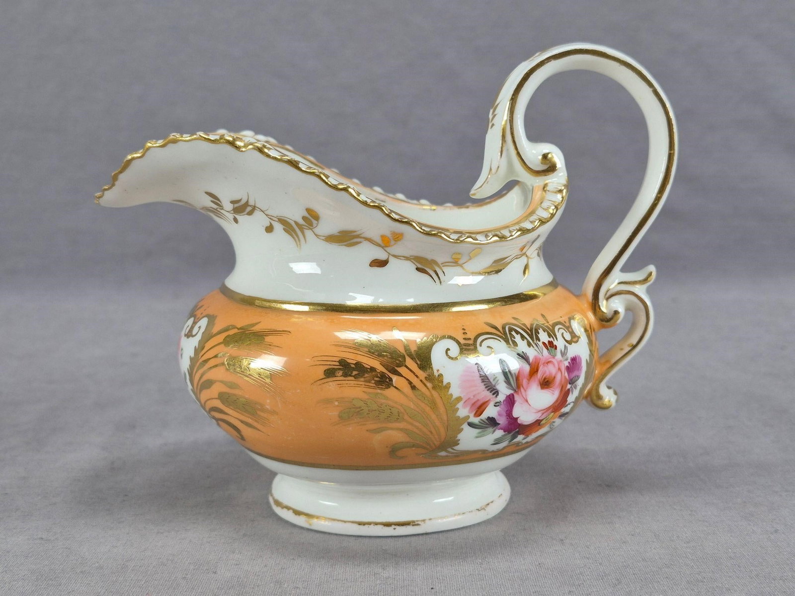 Coalport Hand Painted Apricot Creamer C1820-30s: Antique British bone china gadrooned edge creamer. Decorated with a peach apricot band with hand painted flowers in pink, purple, orange, and white over white framed by gold scrollwork. With a band of