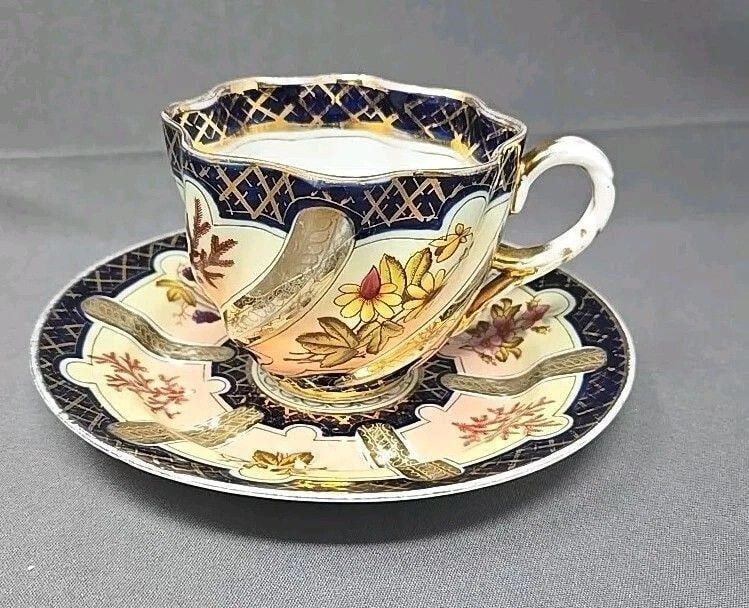 Brothers Schoenau Cup and Saucer Cobalt, Floral: Brothers Schoenau cup and saucer. Cobalt blue with gold, with grapes, flowers, and ferns. Considerable wear to gold. There is a manufacturer defect on saucer foot as shown. There are also light