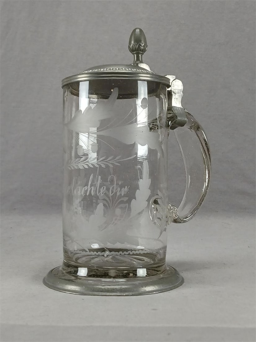 18th Century Freude Lachle Dir Glass Large Stein: Late 18th century blown clear glass stein. Engraved "Freude lachle dir" framed by engraved acorns and leaves. Applied clear glass handle. Rough pontiled base. Pewter mounts at the top and base. The pe