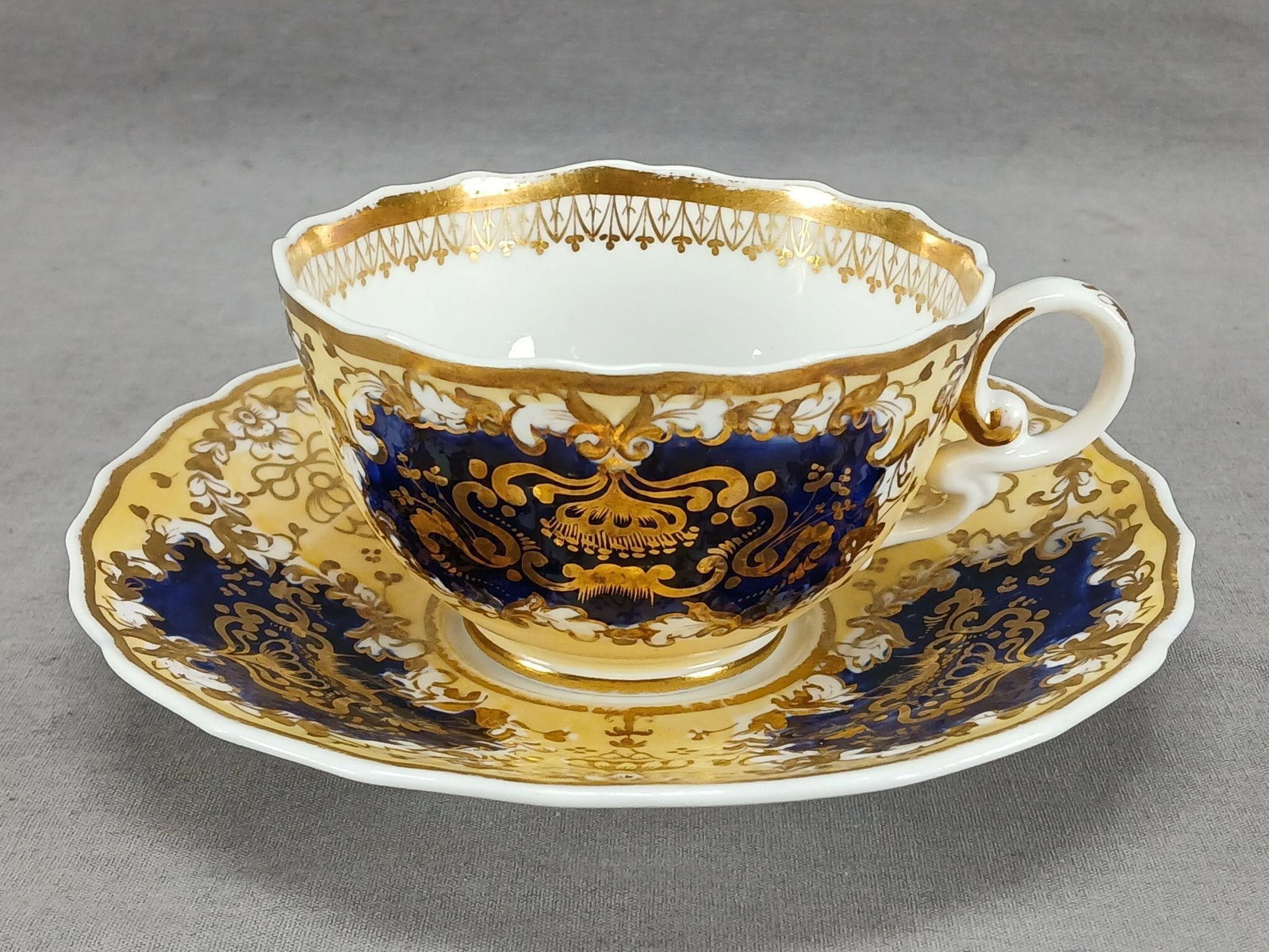 Spode 4440 Floral Scrollwork Tea Cup & Saucer: Antique British bone china tea cup and saucer in the "Sevres embossed" shape with relief molded / embossed floral scrollwork. Decorated with gold cows and floral scrollwork over a cobalt and yellow ba