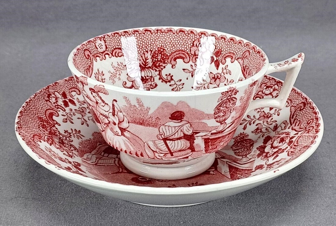 Transferware Watteau Scene Demitasse Cup & Saucer: Rare antique British pearlware demitasse cup and saucer. Decorated with a red transfer pattern depicting Renaissance era gentlemen and a lady playing a guitar. Floral and scrollwork border. The