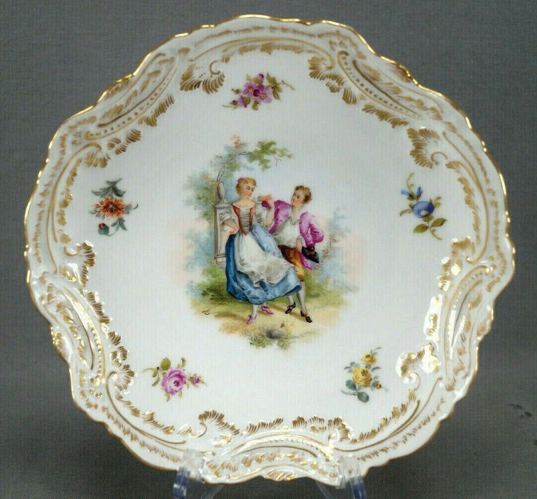 Dresden Hand Painted Courting Couple Shallow Bowl: Antique German porcelain shallow bowl with relief molded scrollwork and leaf designs with gold gilt highlights along the edge. Decorated with a hand painted courting couple in the center with a monume