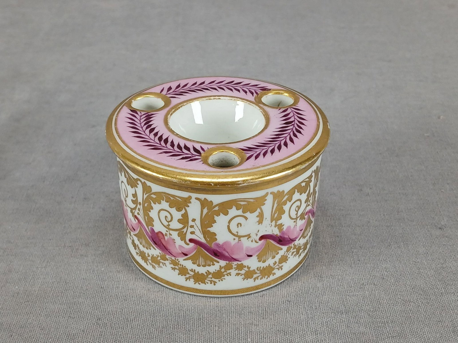 English Hand Painted Drum Shape Porcelain Inkwell: Antique English porcelain drum shape inkwell. Decorated with hand painted puce, pink, and gold floral scrollwork and gold floral swags along the sides. With purple leaves over pink along the top. Gold