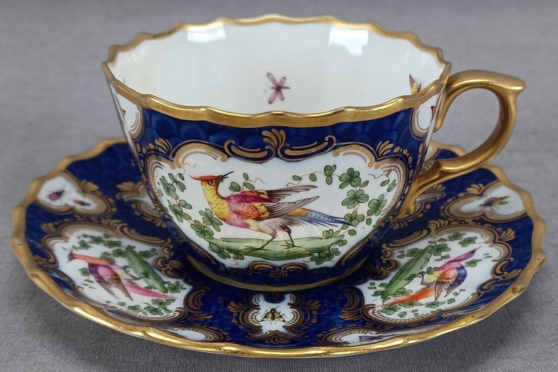 Copeland Hand Painted Birds Cobalt Cup & Saucer B: Antique British bone china cup and saucer. Decorated with hand painted Chelsea birds and insects in pink, purple, blue, yellow, orange, and white framed in gold scrollwork. Has a cobalt fishscale type