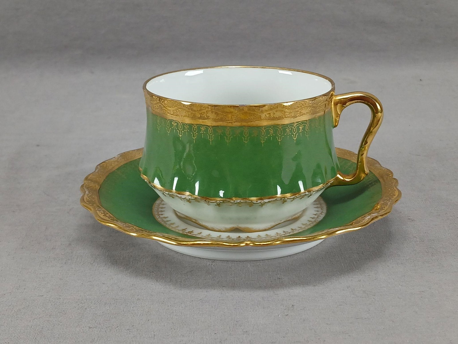Limoges Green & Gold Encrusted Tea Cup & Saucer C: Antique French porcelain tea cup and saucer. Decorated with a green border with gold scrollwork overlay. Gold encrusted floral band around the edge. Gold gilding to the handle. Marked Limoges France w